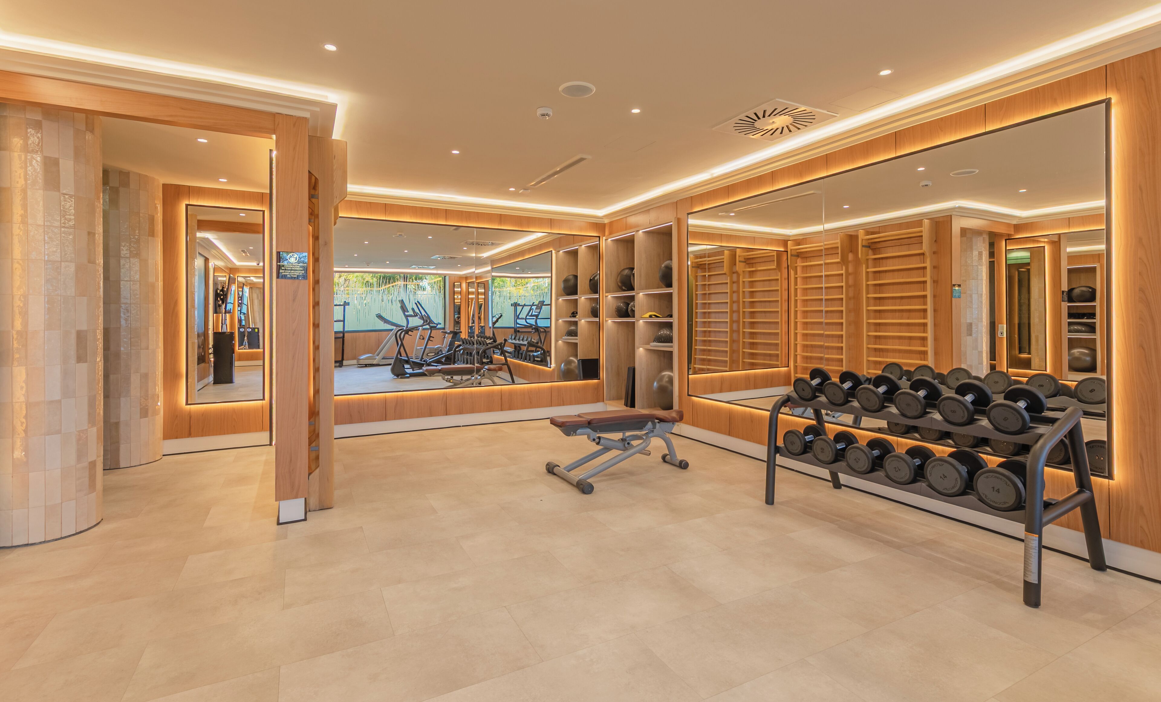 Un gimnasio moderno con equipo de ejercicio, espejos y una barra de mancuernas.