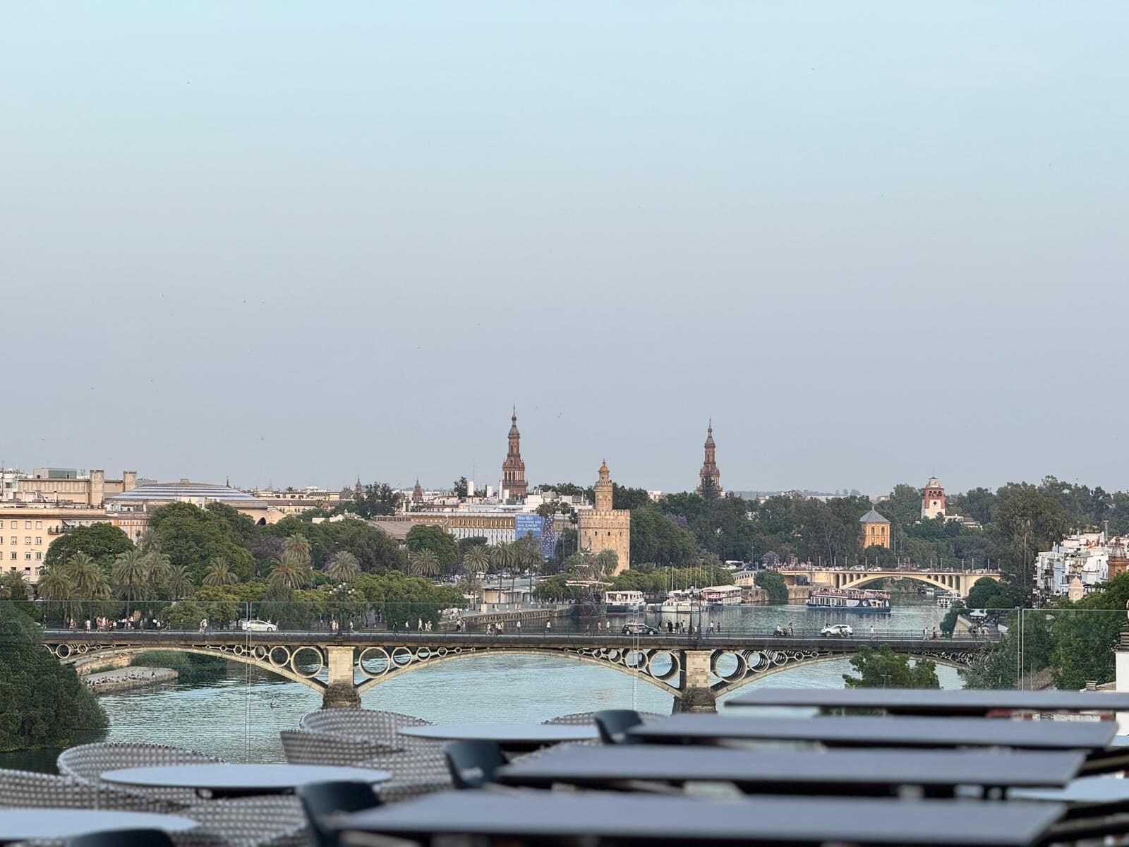 Vista a la orilla del río con un puente, edificios históricos y una torre al fondo.