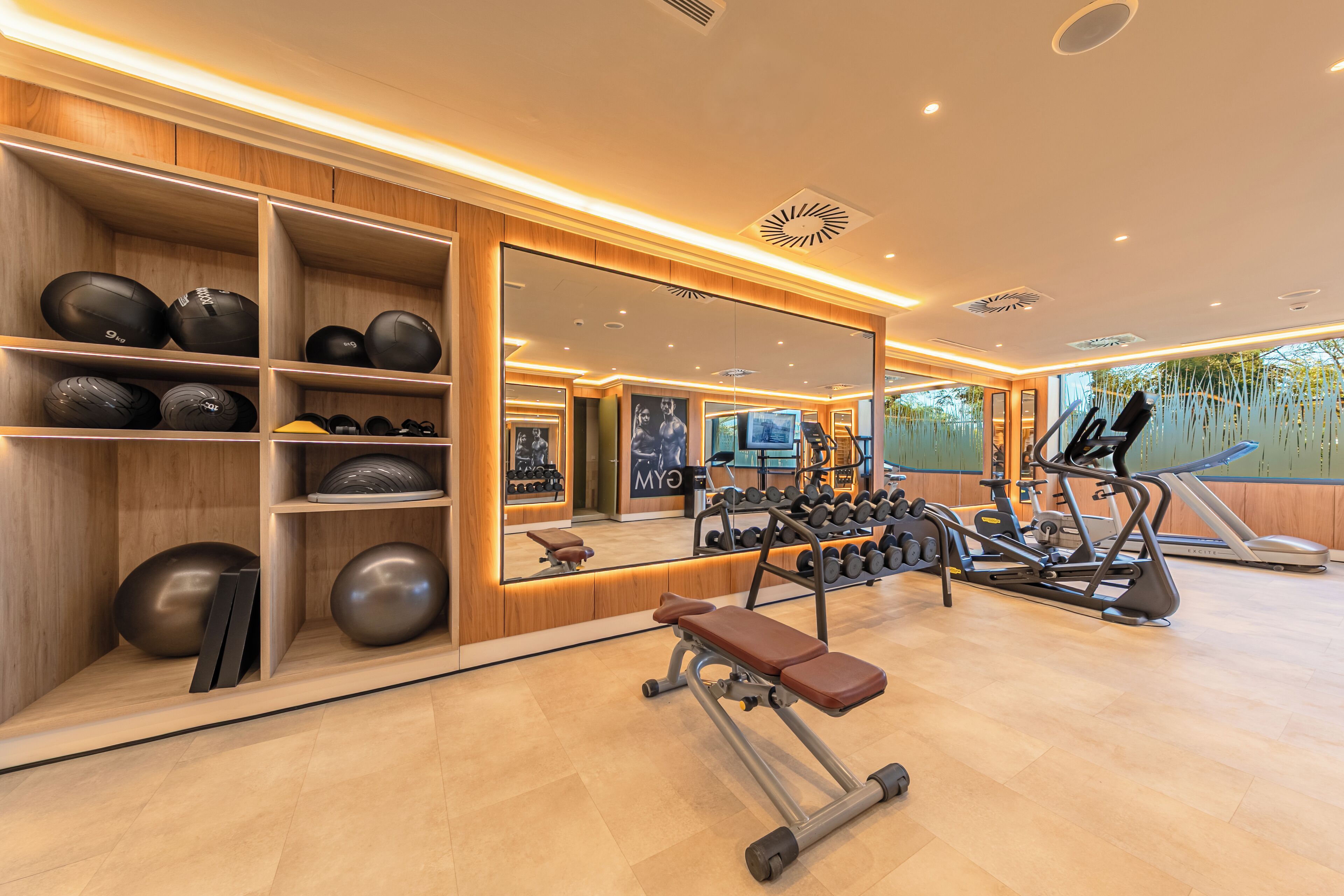A gym with exercise equipment, a bench, and a mirrored wall.