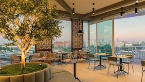 Un restaurante moderno con un gran árbol, techos altos y amplios ventanales que ofrecen vistas a la ciudad.