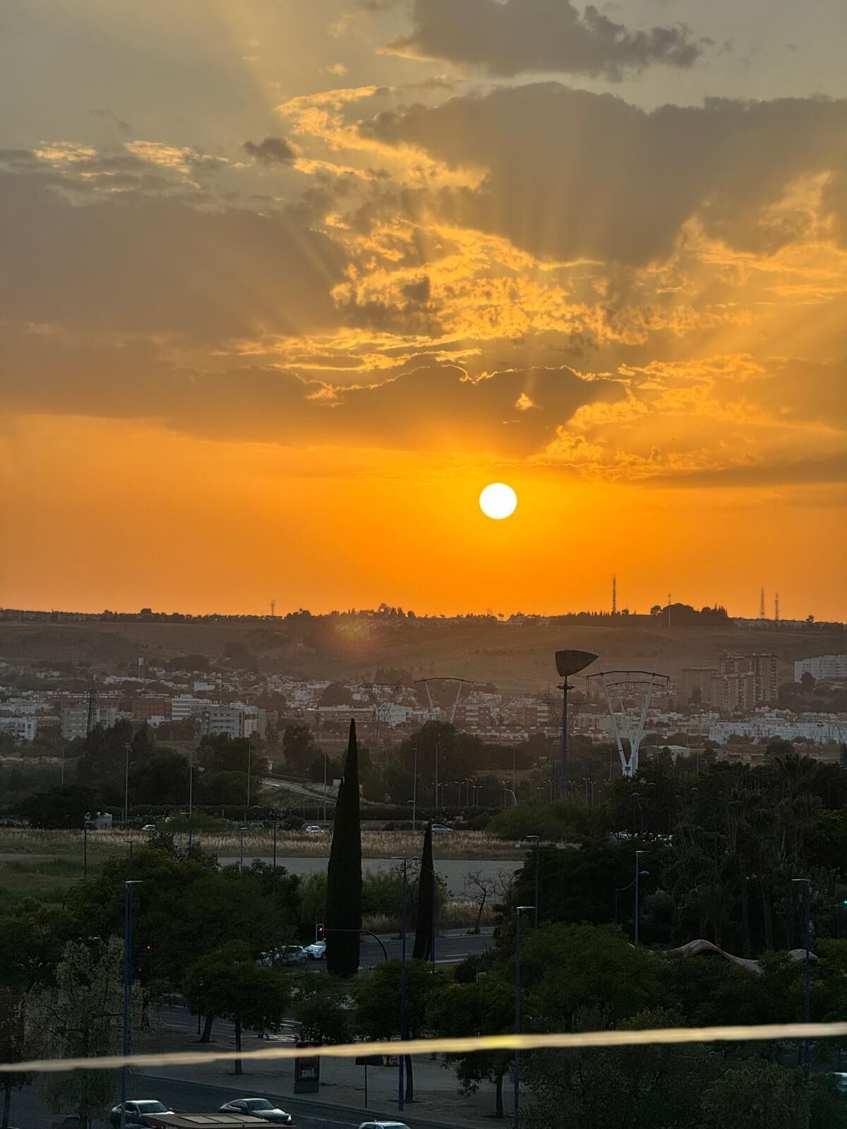 Un atardecer sobre un paisaje urbano con edificios, árboles y una torre destacada.