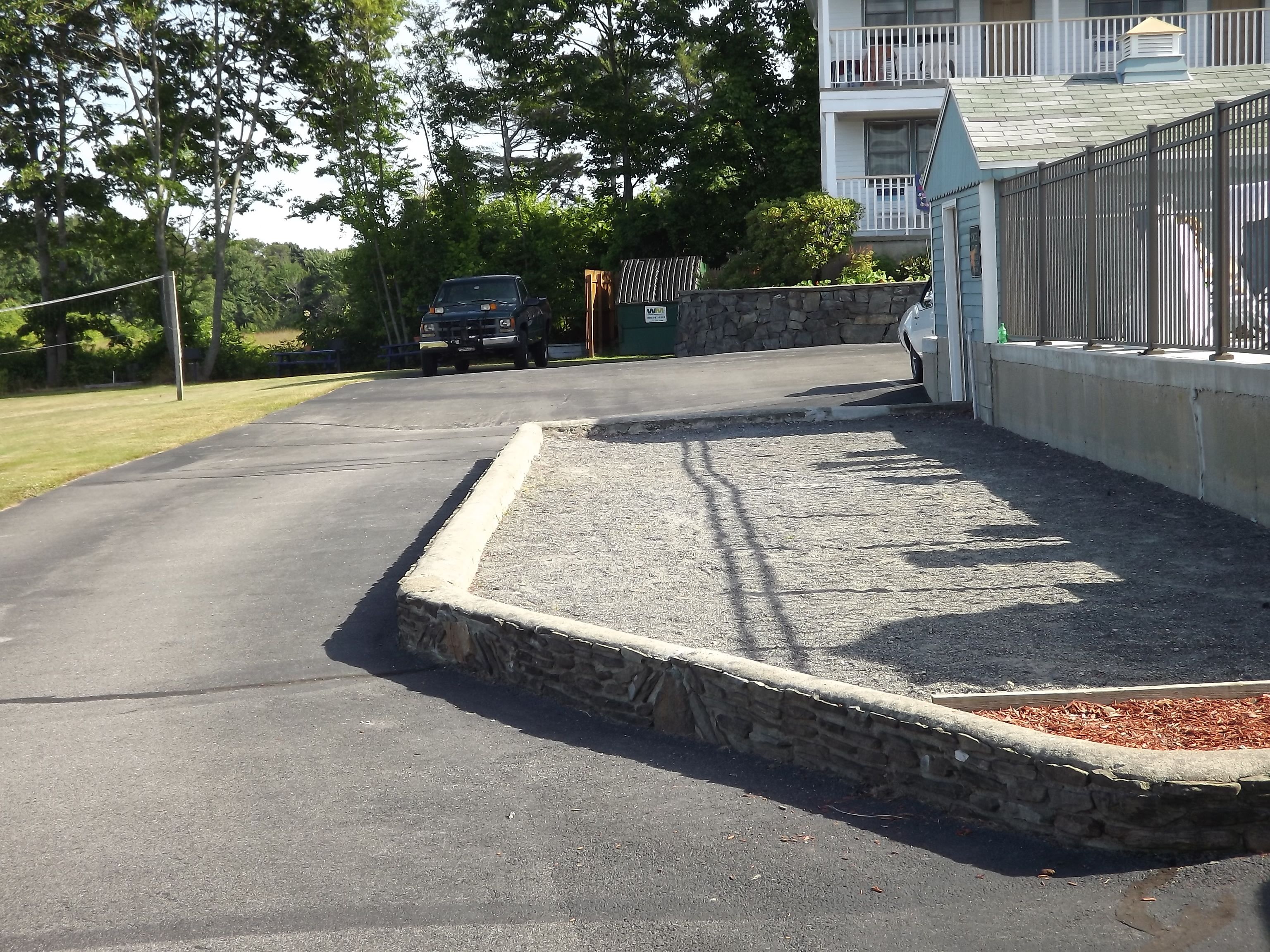 A paved driveway leading to a gated entrance with a stone wall and a gravel area.