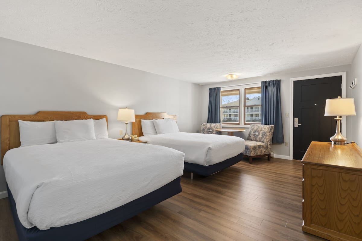 A hotel room with two beds, a small table, a chair, and a wooden dresser.