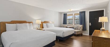 A hotel room with two beds, a small table, a chair, and a wooden dresser.