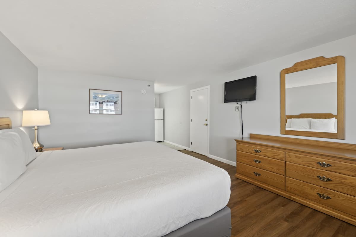 A bedroom with a large bed, a wooden dresser, a television, and a framed picture on the wall.