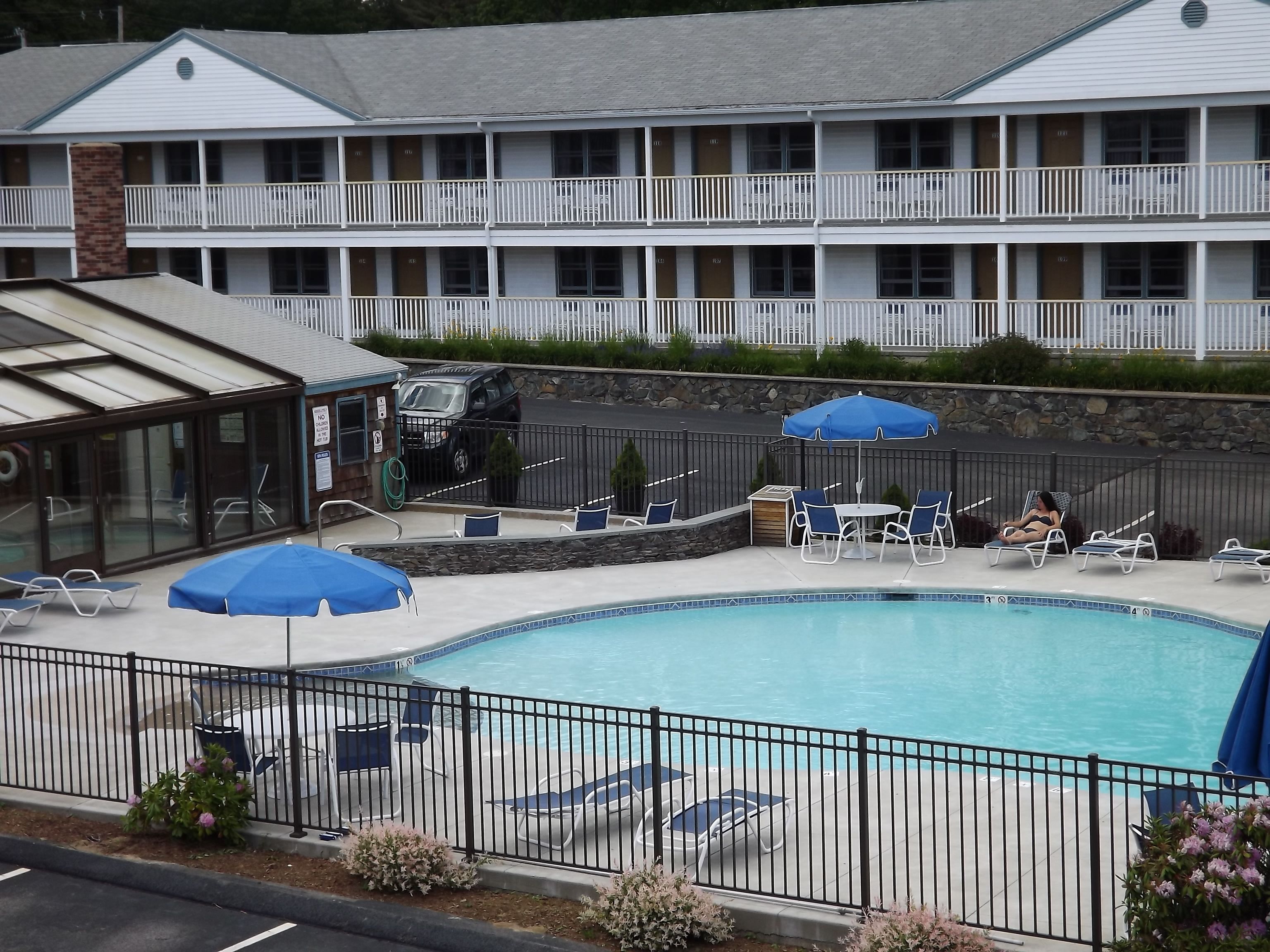 A hotel with a swimming pool, lounge chairs, and umbrellas.