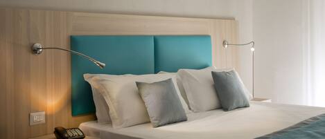 A hotel room with a wooden headboard, a teal accent wall, a bed with white bedding, and a bedside table with a telephone and remote control.