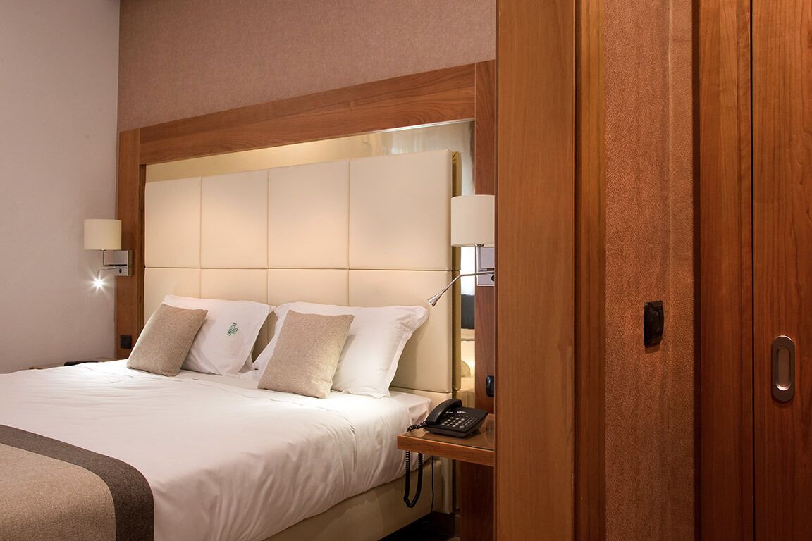 Una habitación de hotel con una cama grande, una mesita de noche con lámpara y un armario de madera.