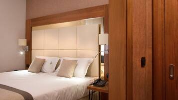 Una habitación de hotel con una cama grande, una mesita de noche con lámpara y un armario de madera.