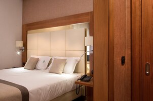 Una habitación de hotel con una cama grande, una mesita de noche con lámpara y un armario de madera.