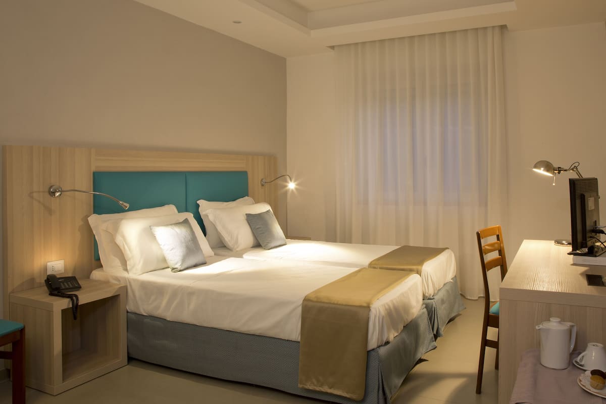 A hotel room with a large bed, bedside lamps, a desk with a chair, and a telephone.