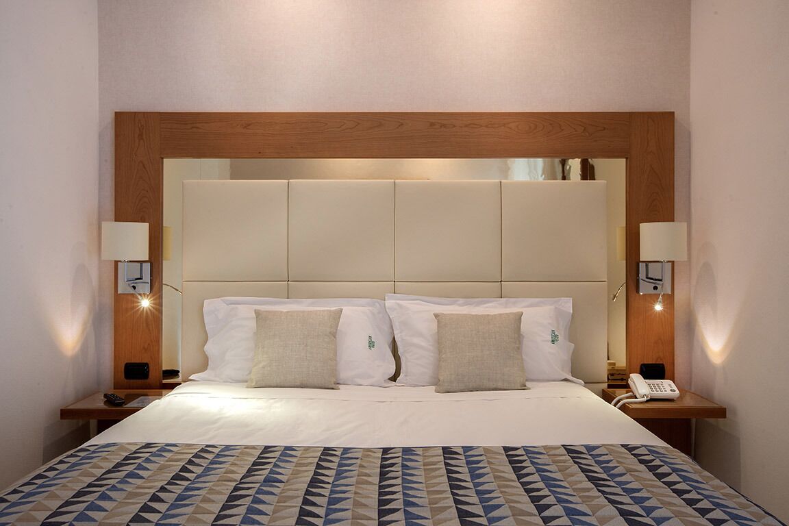 Ein Hotelzimmer mit einem großen Bett, zwei Nachttischen mit Lampen und einem hölzernen Kopfteil.