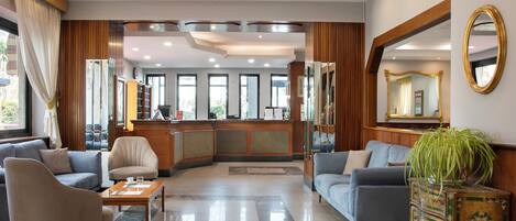 Un vestíbulo de hotel con recepción, zona de estar y grandes ventanales.