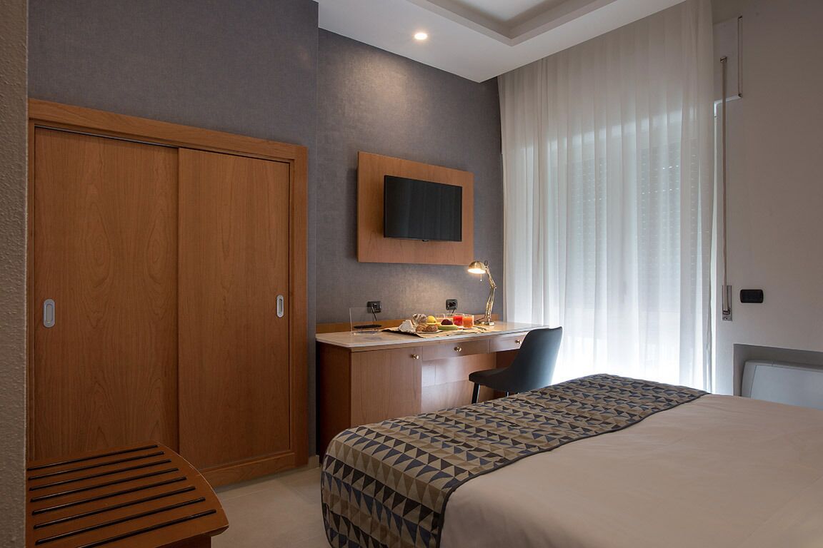 A hotel room with a bed, desk, and wardrobe.