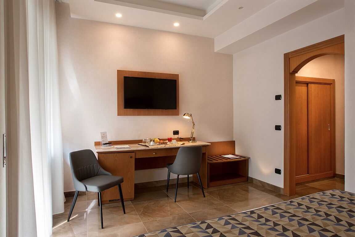 A modern room with a desk, two chairs, a television mounted on the wall, and a wooden wardrobe.