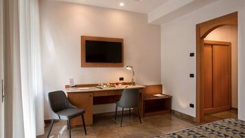 A modern room with a desk, two chairs, a television mounted on the wall, and a wooden wardrobe.