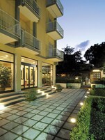 Un hotel de varios pisos con una entrada bien iluminada, un área de estar al aire libre y un jardín ajardinado.