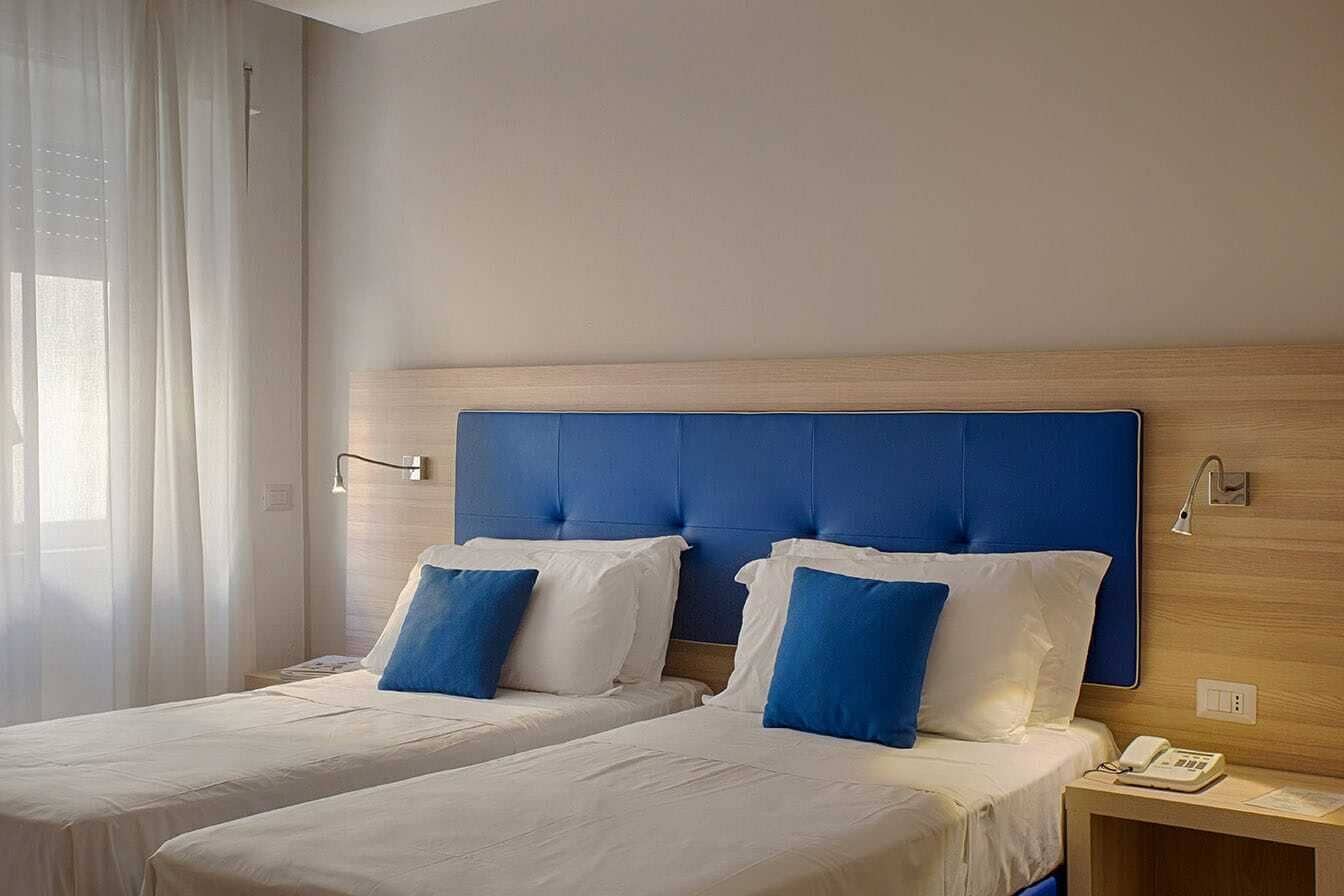 Habitació d'hotel amb dos llits, un amb un capçal de fusta, roba de llit blanca i una taula de nit amb una làmpada i un telèfon.