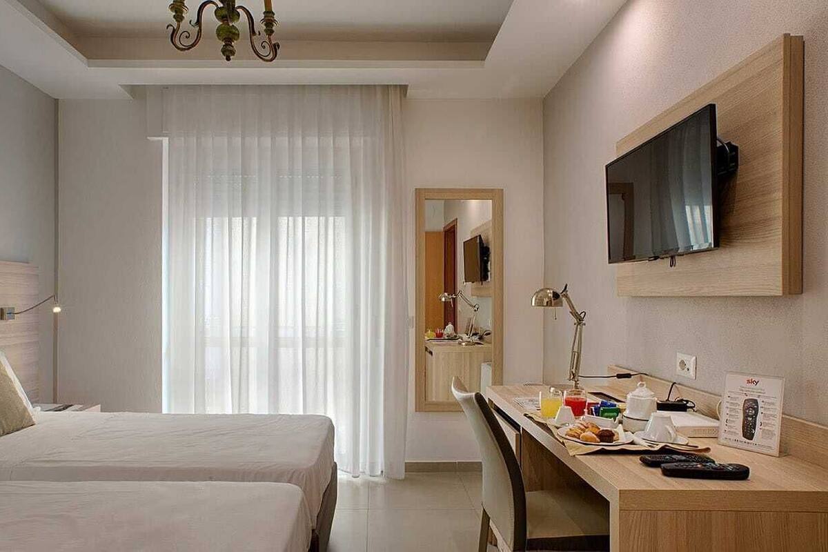 A hotel room with two beds, a desk with breakfast items, a TV, and a mirror.