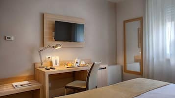 Habitación de hotel con cama, escritorio, silla, televisor, espejo y ventana con cortinas.