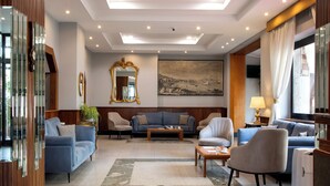 A spacious living area with a blue sofa set, a coffee table, and a large painting on the wall. - American Hotel (Pozzuoli)