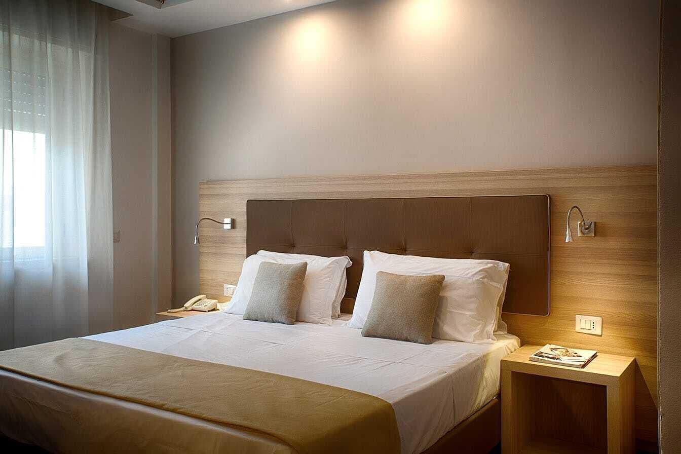 Une chambre d’hôtel avec un grand lit, deux tables de chevet, une petite table et une fenêtre avec des rideaux.