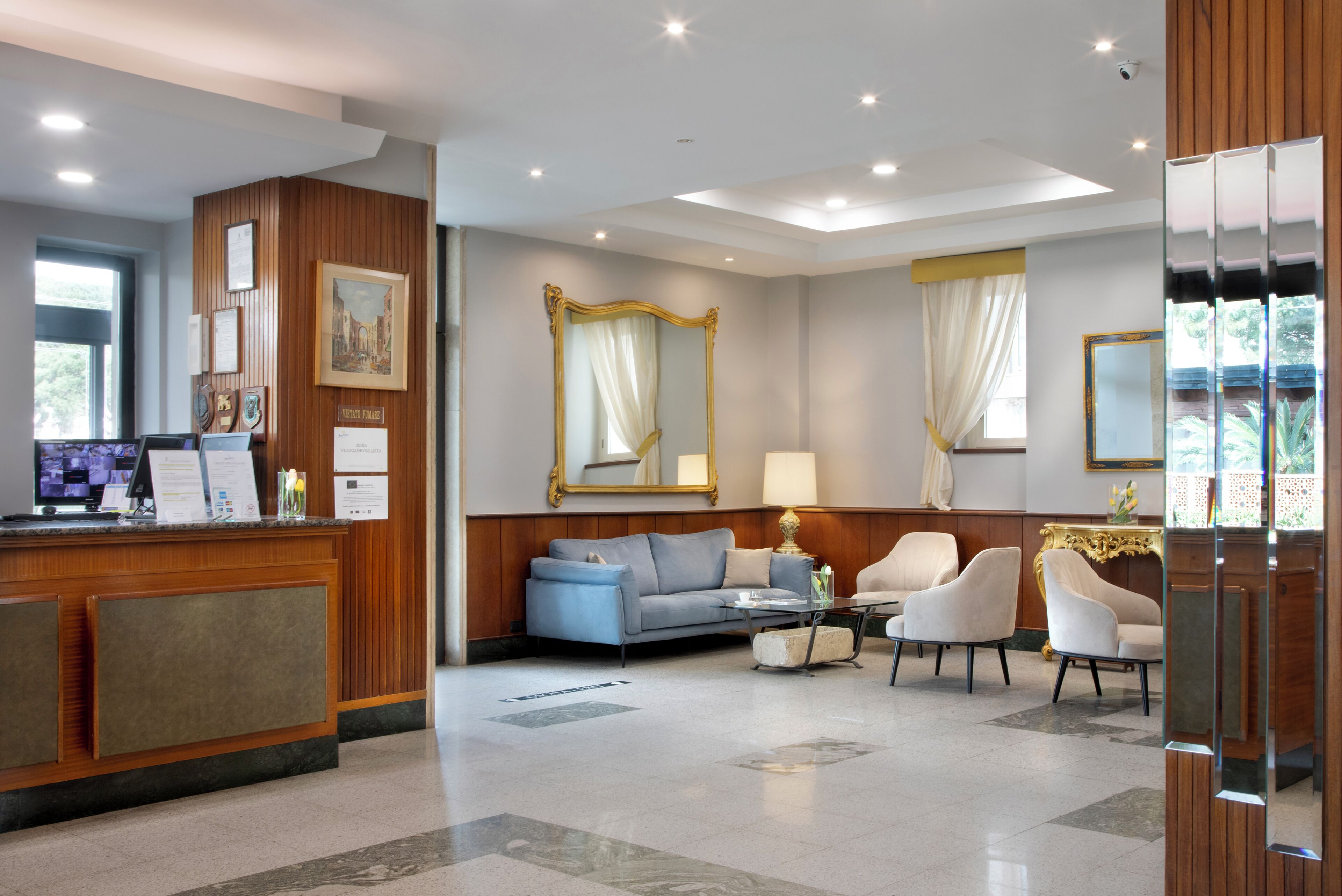 Een hotelhal met een receptiebalie, een zithoek en een grote spiegel.