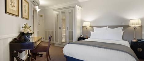 A hotel room with a large bed, bedside lamps, a desk with a vase of flowers, and a wardrobe.