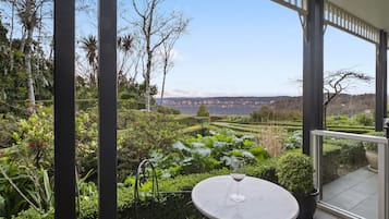 Une terrasse avec une table et des chaises, un pot de fleurs et une vue sur un jardin aménagé et des montagnes lointaines.
