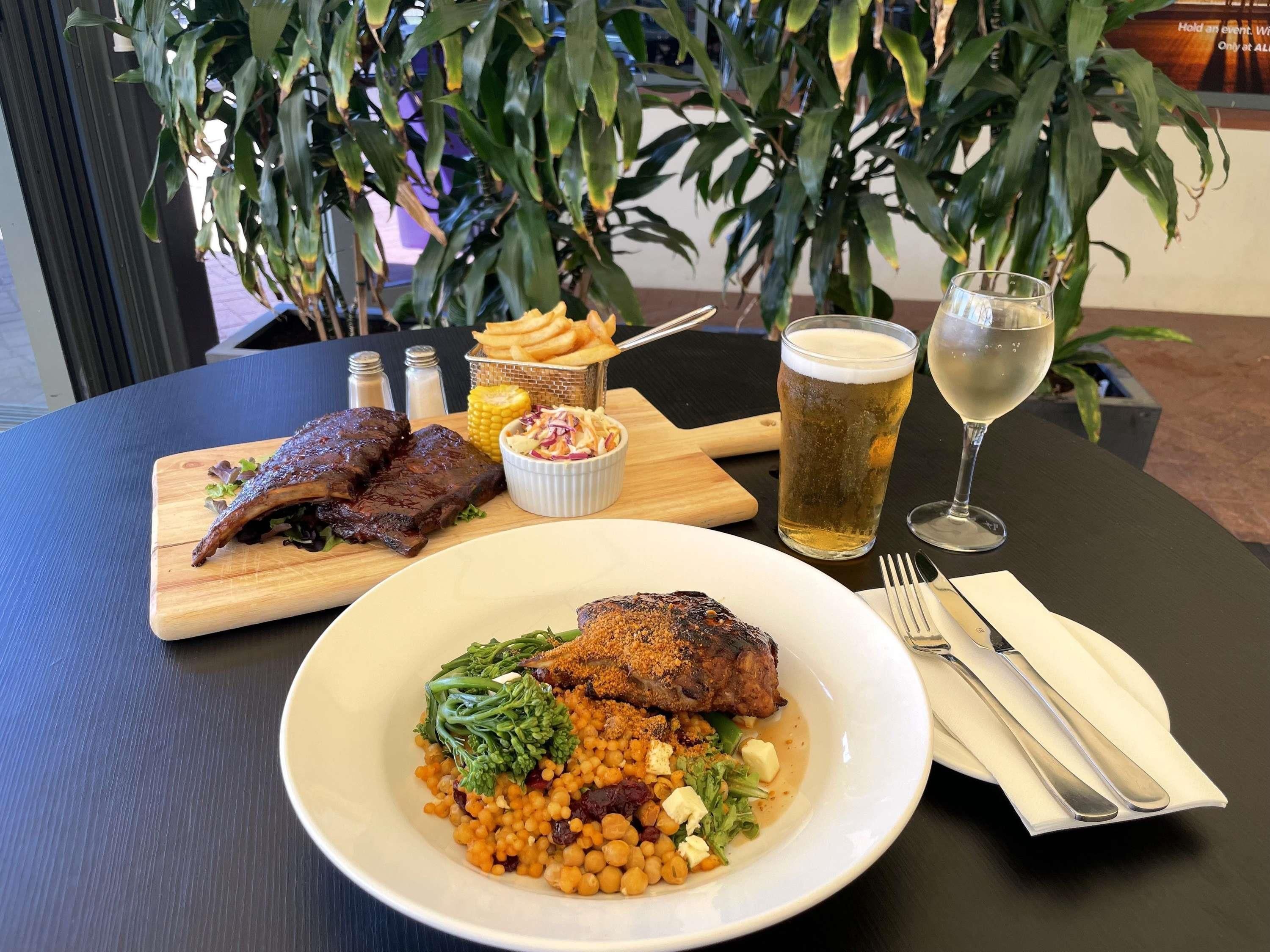 A dining table with a meal consisting of grilled meat, a bowl of salad, and a glass of beer.
