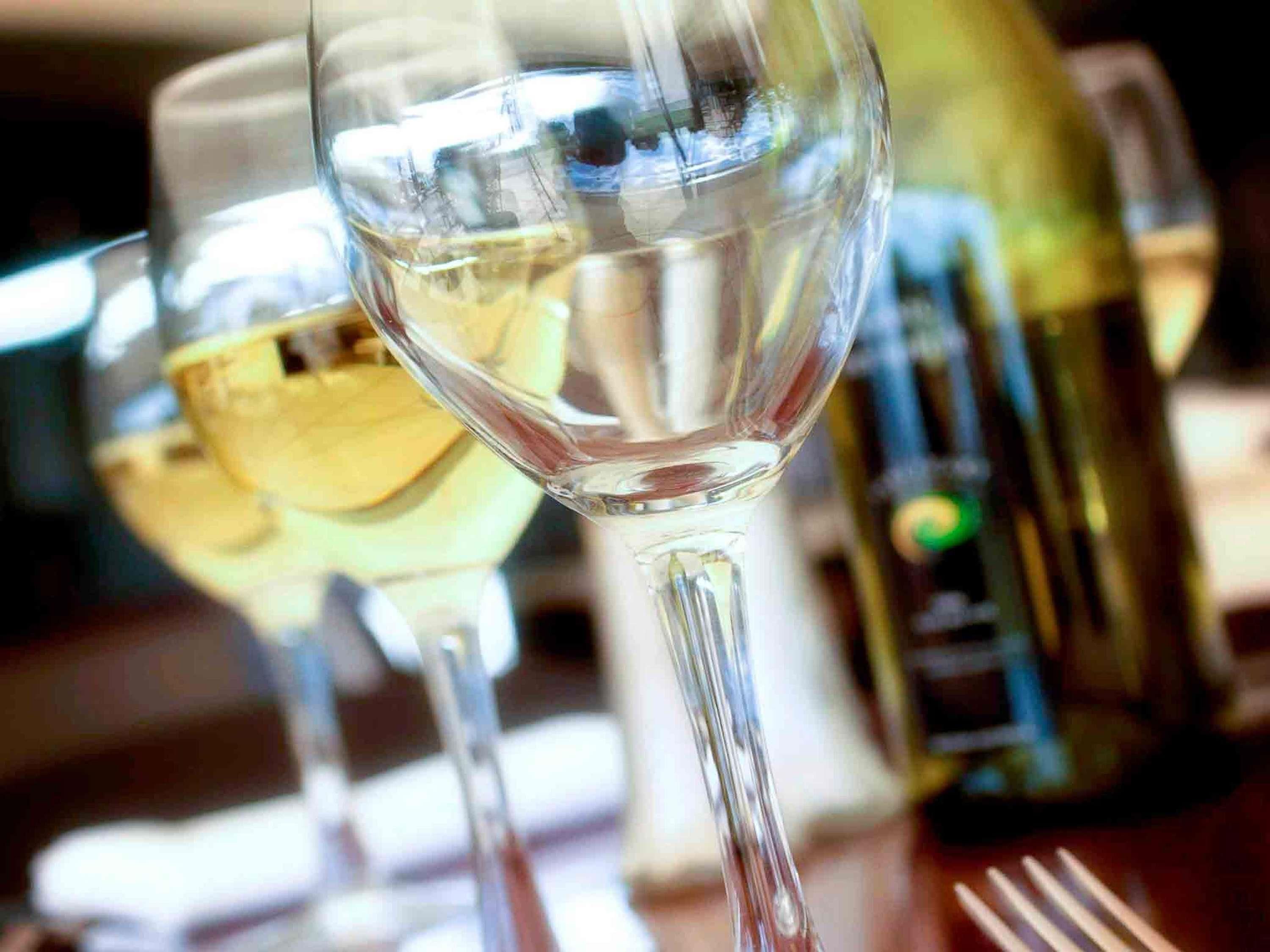 Gros plan sur un verre à vin contenant un liquide clair, vraisemblablement du vin, et une bouteille de vin en arrière-plan.