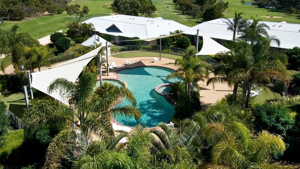 Un complexe hôtelier doté d’une piscine, de palmiers et, au loin, d’un terrain de golf.