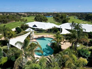 A resort with a swimming pool, palm trees, and a golf course in the background. - Mercure Bunbury Sanctuary Golf Resort (Pelican Point)