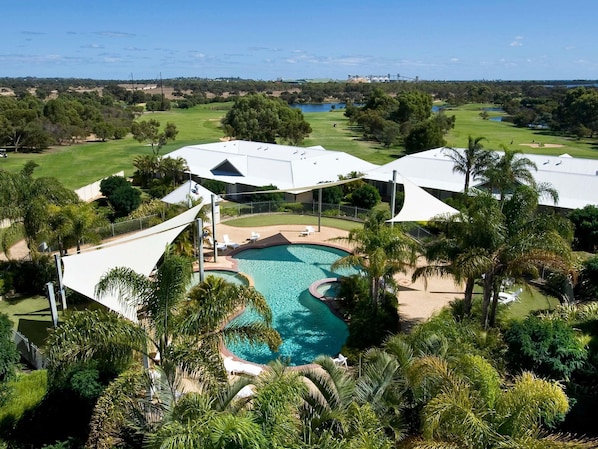 A resort with a swimming pool, palm trees, and a golf course in the background.