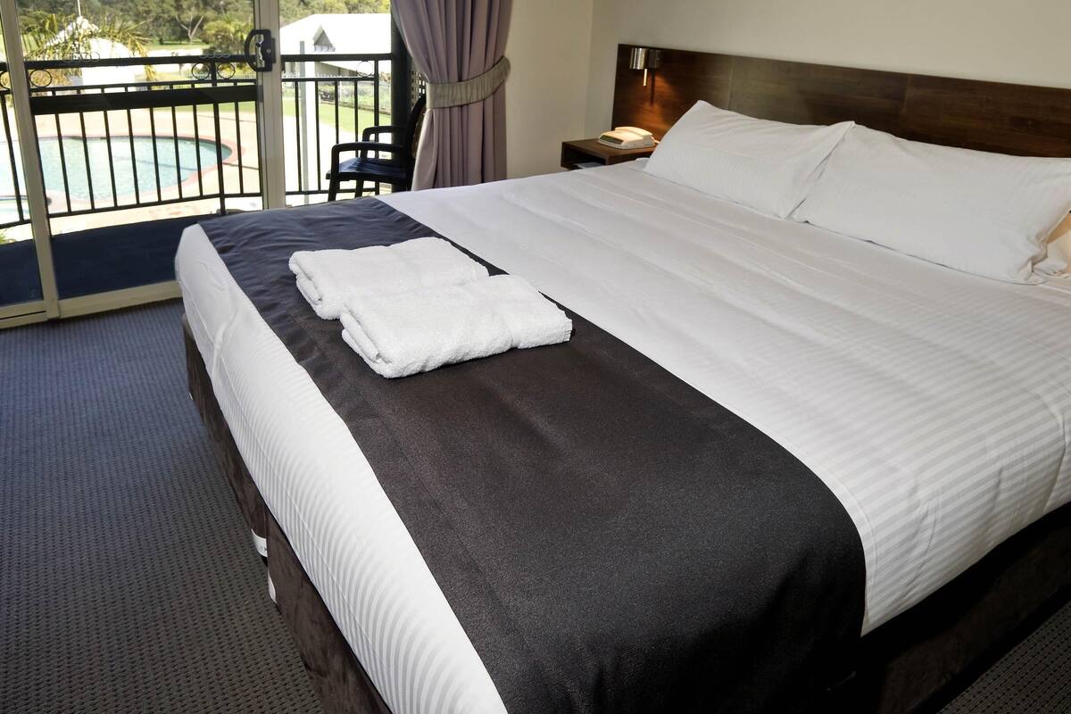 Habitación de hotel con cama, mesita de noche, una silla, vista a una piscina y un balcón.