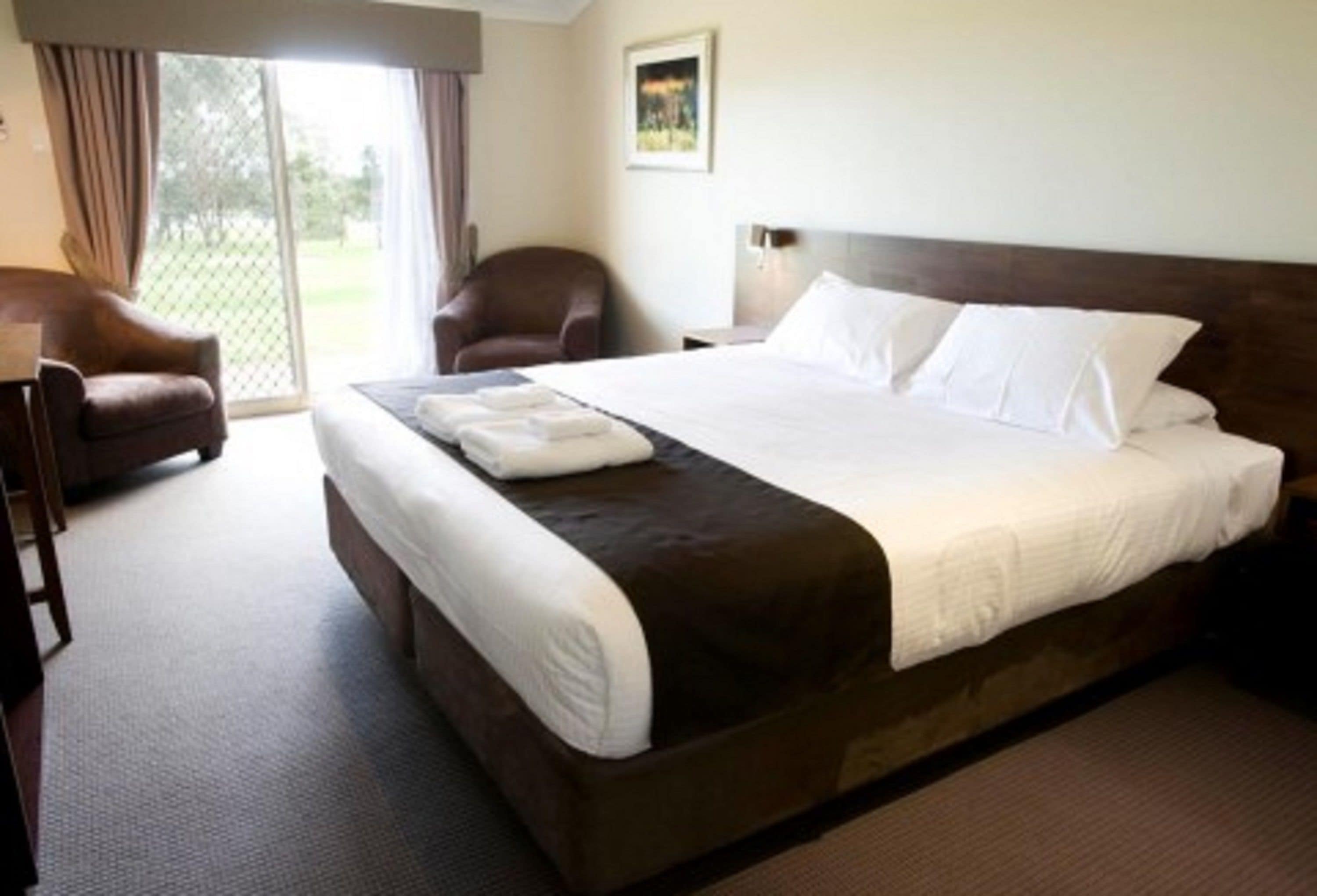 A hotel room with a large bed, a chair, a desk, and a view of the outdoors through a sliding door.