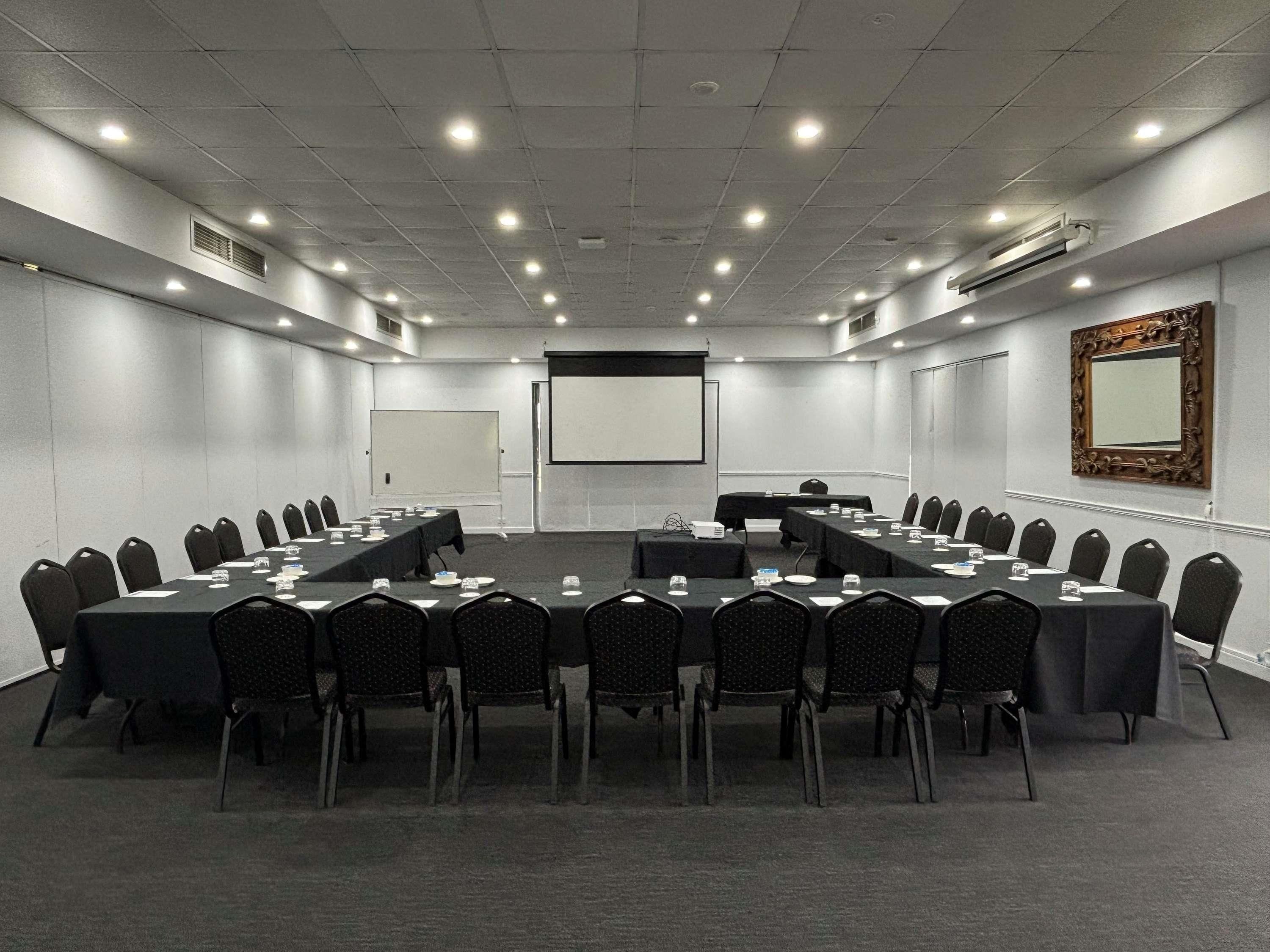 A conference room with a long table, chairs, a projector screen, and a whiteboard.