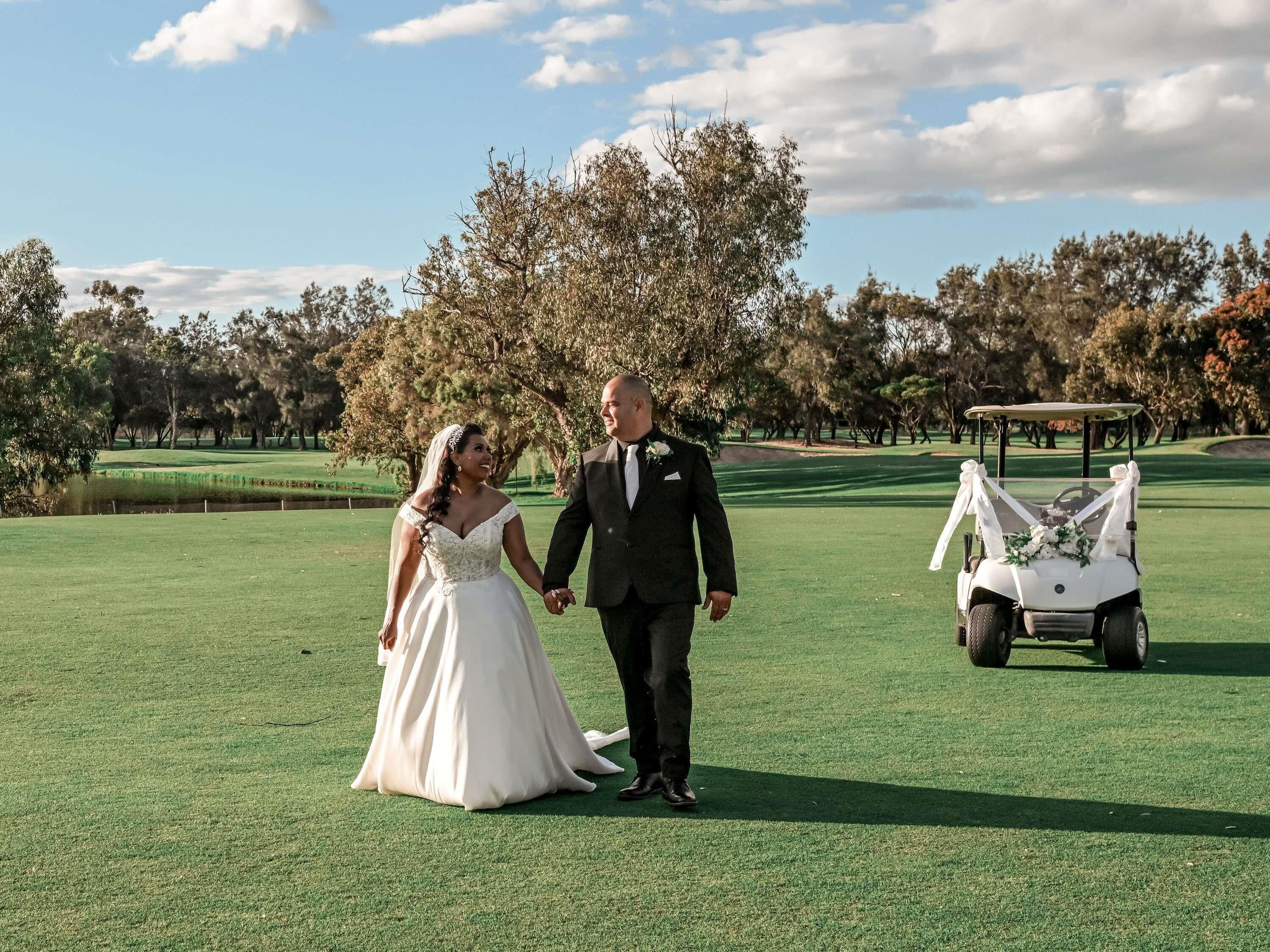 A couple holding hands on a golf course with a golf cart in the background.