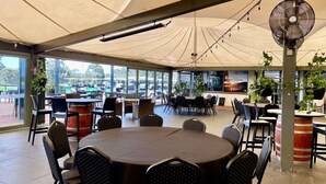 Un espace de restauration intérieur avec des tables rondes, des chaises, des ventilateurs de plafond et de grandes fenêtres.