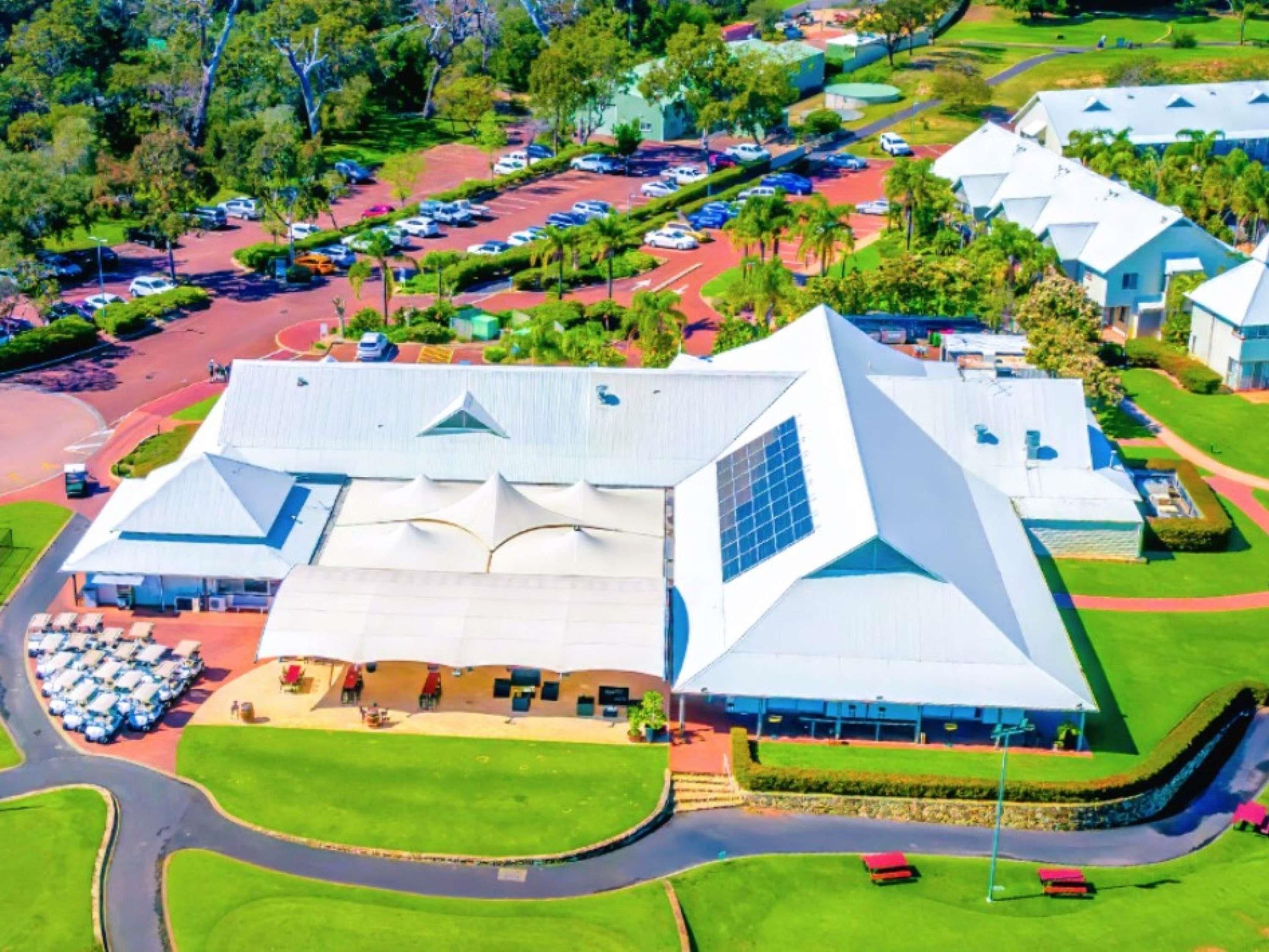 An aerial view of a modern hotel with a unique geometric roof design, surrounded by lush greenery and a parking lot.