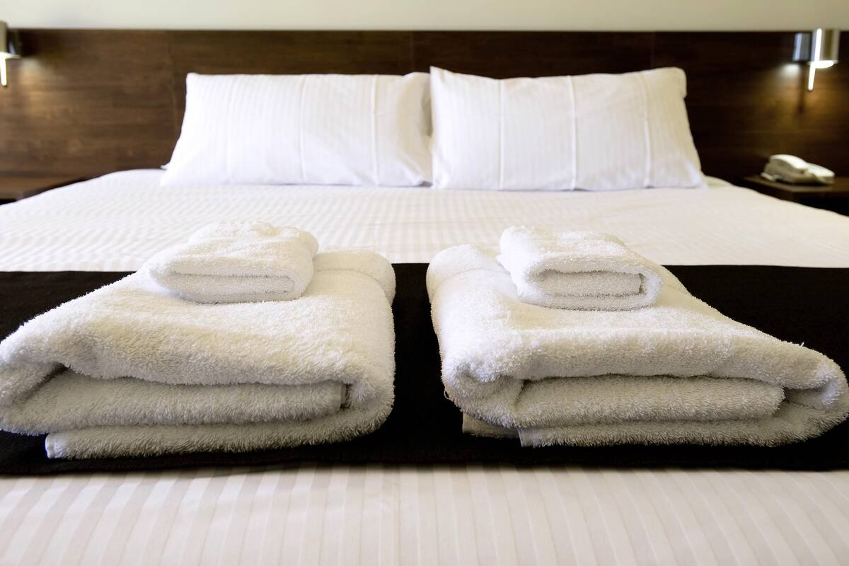 Habitación de hotel con una cama bien hecha, dos toallas dobladas sobre la cama y una mesita de noche con un teléfono.