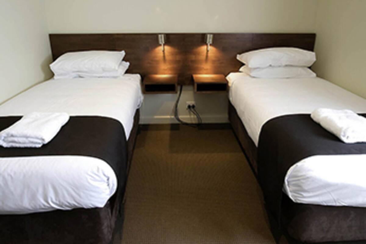 Una habitación de hotel con dos camas individuales, cada una con una almohada y una toalla doblada.