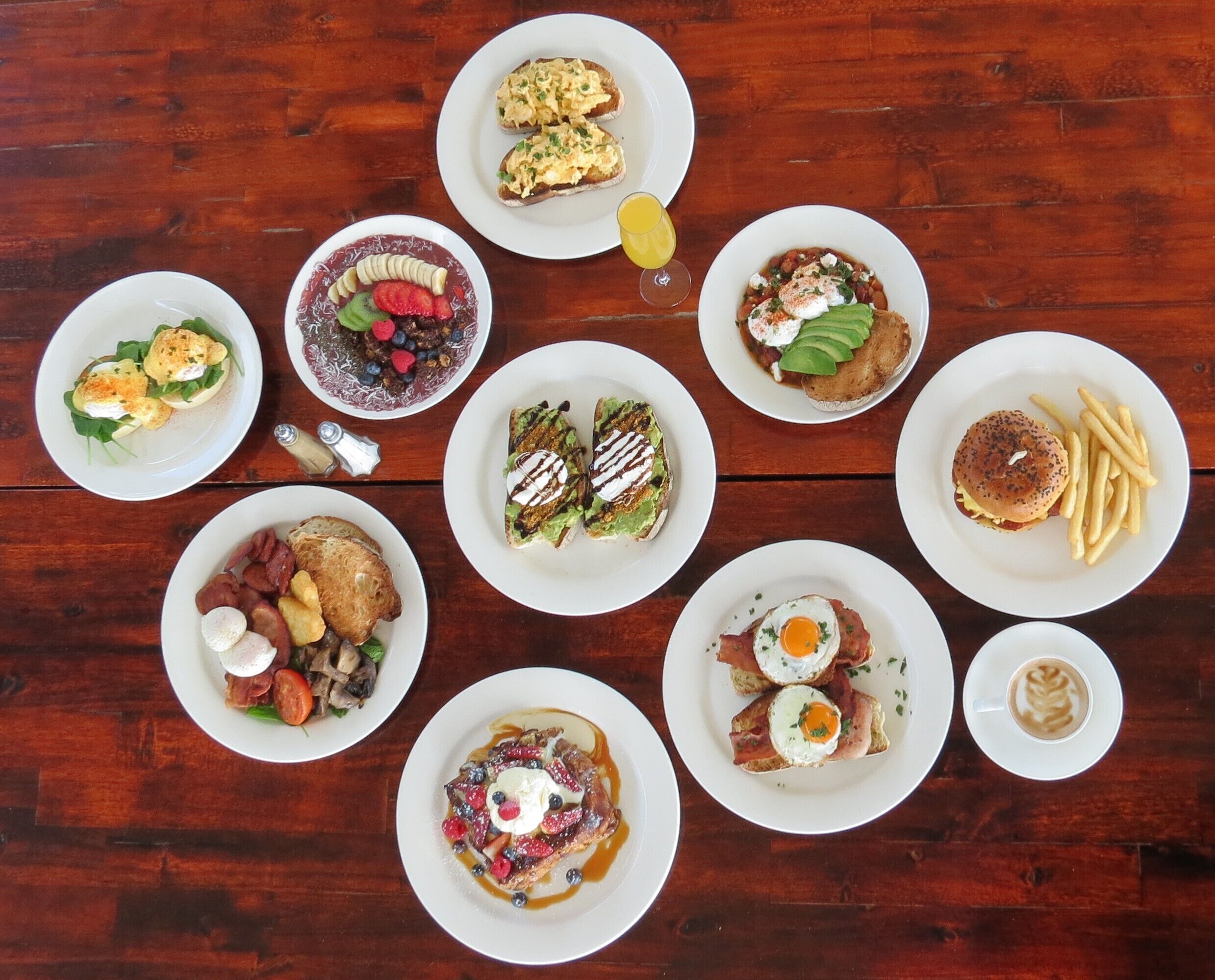 Variedad de platos de desayuno sobre bandejas blancas dispuestas sobre una mesa de madera.