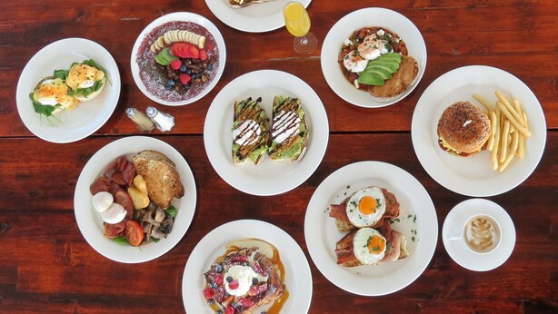 Variedad de platos de desayuno sobre bandejas blancas dispuestas sobre una mesa de madera.