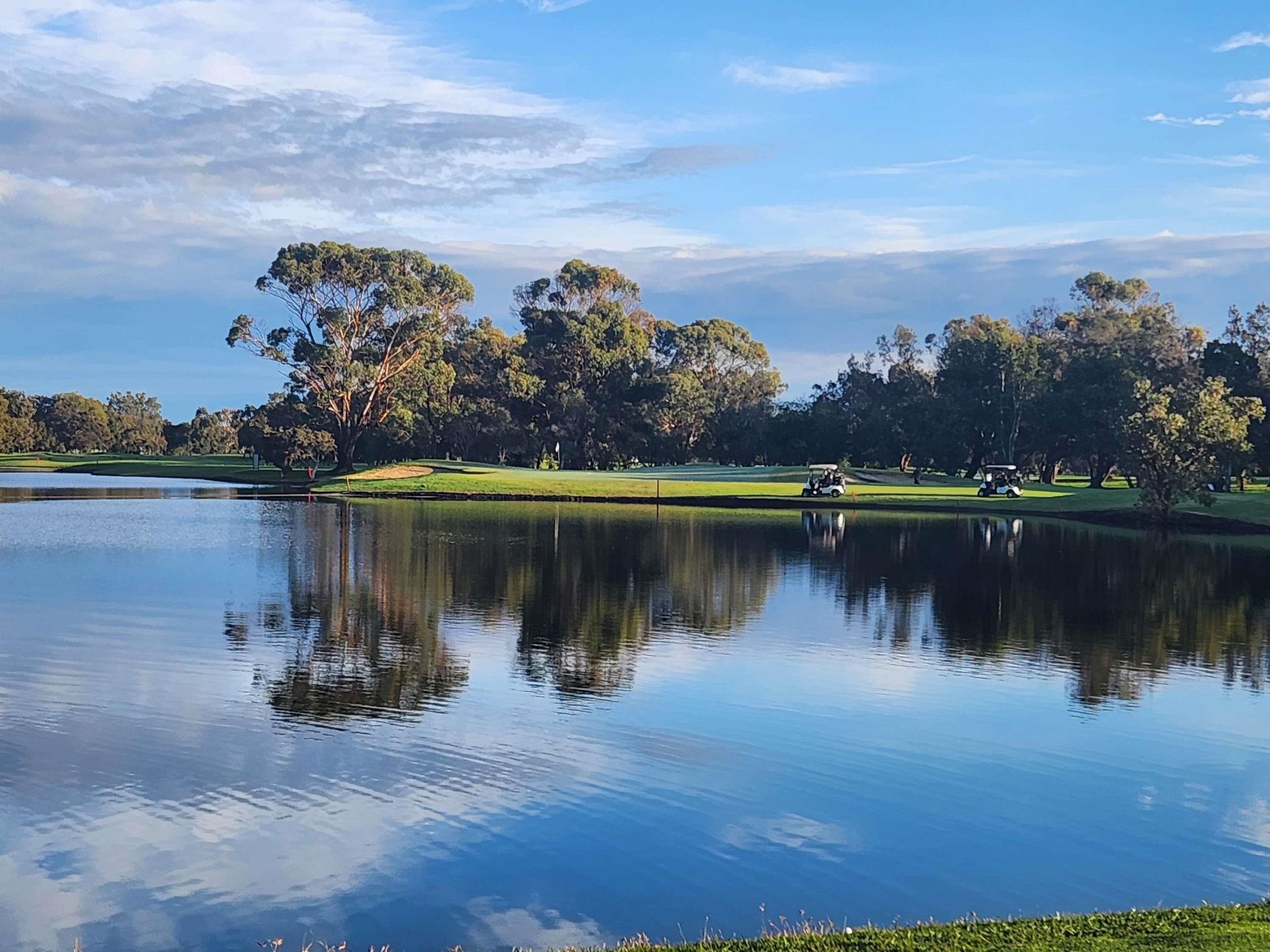Een rustige golfbaan met een vijver die bomen weerspiegelt en een heldere lucht.