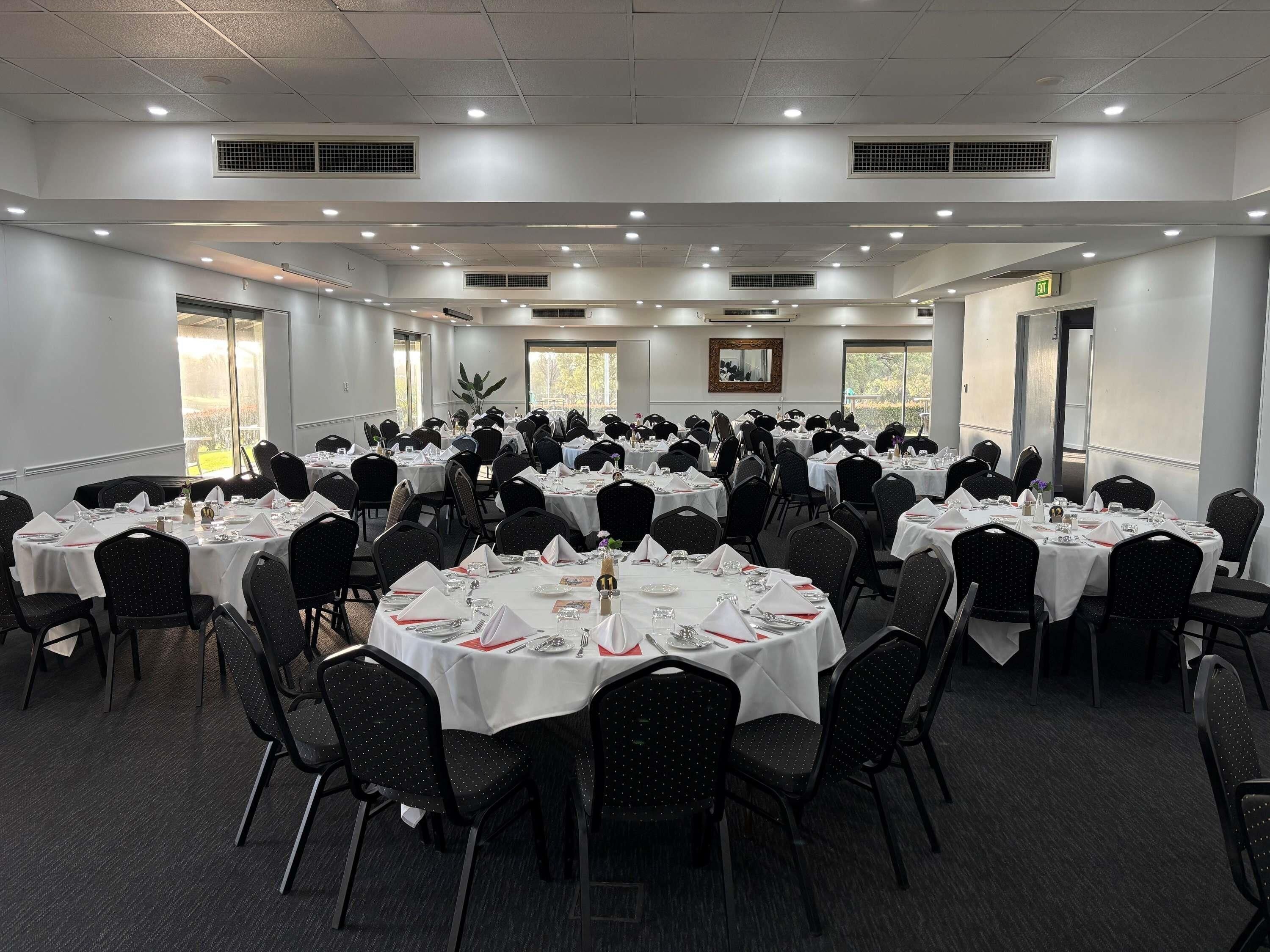 A large conference room with round tables, black chairs, white tablecloths, and ceiling lights.