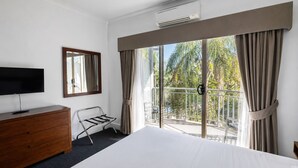 A hotel room with a bed, a TV on a wooden dresser, a balcony with curtains, and a view of palm trees. - Mercure Bunbury Sanctuary Golf Resort (Pelican Point)