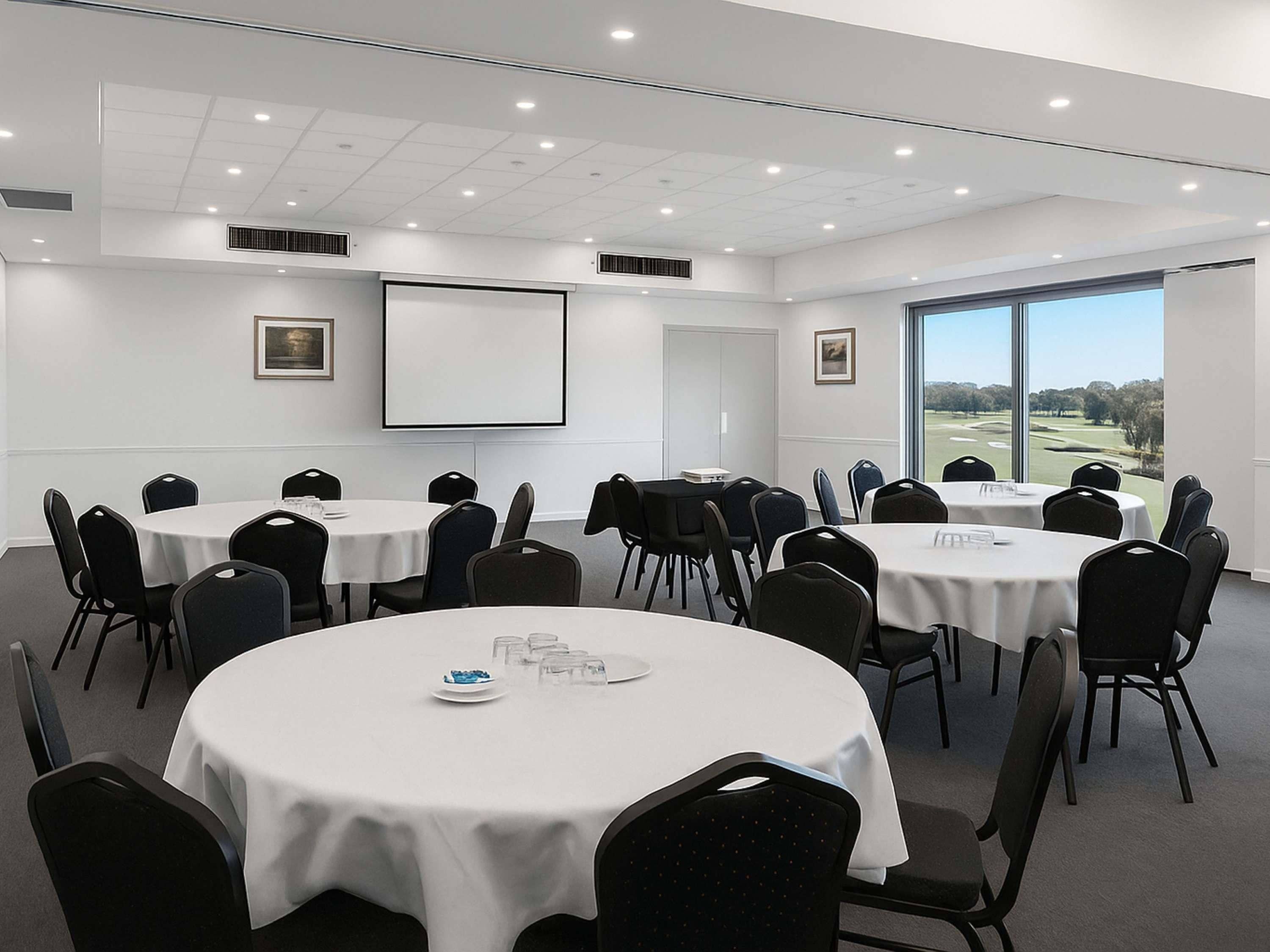 A conference room with multiple tables and chairs, large windows with a view of a golf course, and a whiteboard on the wall.