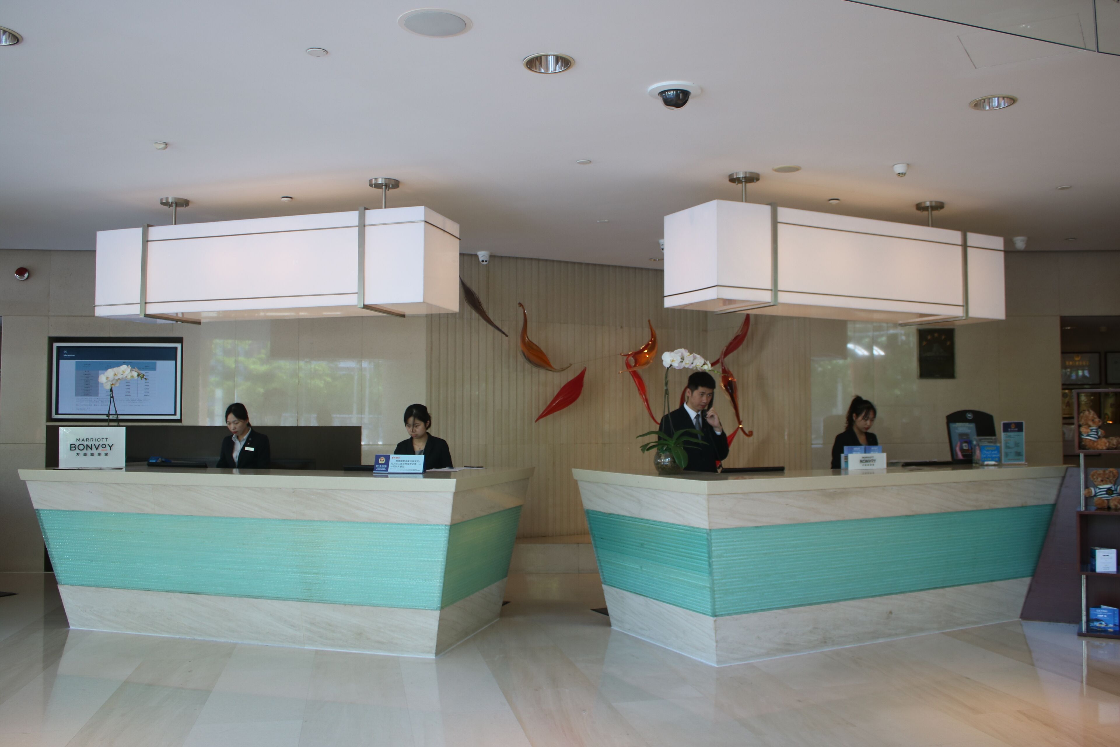 A hotel reception area with two reception desks, a digital screen, and a wall-mounted security camera.
