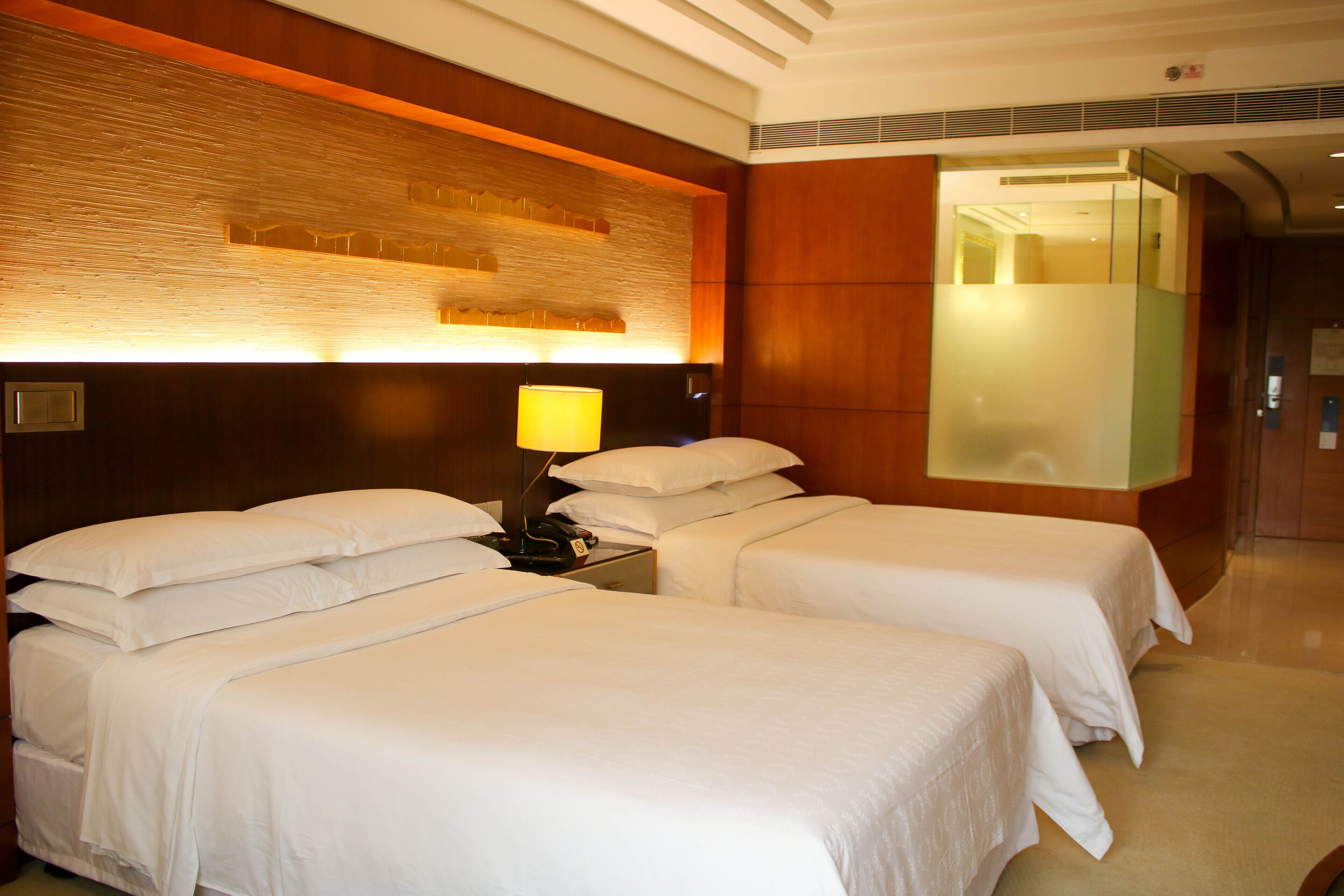 A hotel room with two single beds, a nightstand with a lamp, and a wooden accent wall.